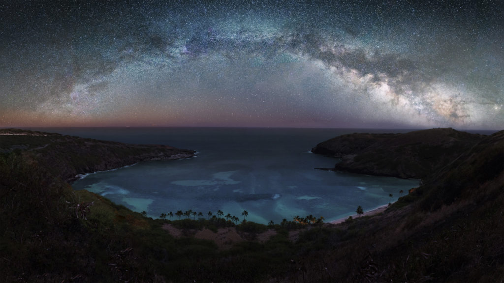 Hanauma Bay as seen from the summit ridge at night with the Milky Way in the sky above the water.